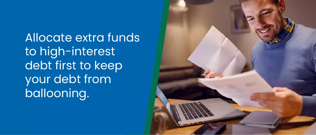 Allocate extra funds to high-interest debt first to keep your debt from ballooning - Man looking at papers in front of his laptop